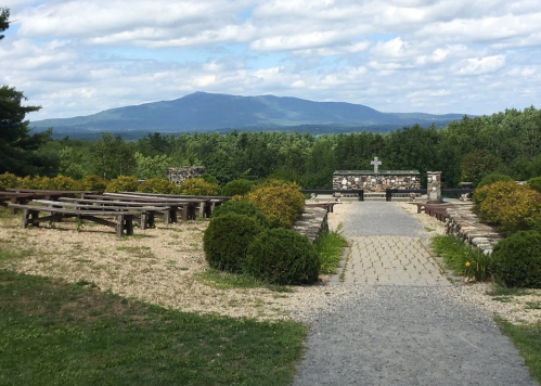 A scenic view of a pathway leading to a stone altar, surrounded by greenery and mountains in the background.