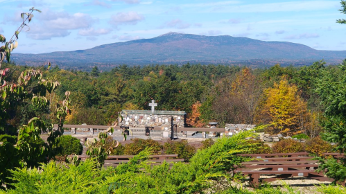 A scenic view of a mountain surrounded by colorful autumn foliage and a stone cross in the foreground.