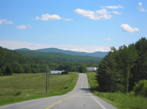 A winding road leads through a green landscape with mountains in the background under a clear blue sky.
