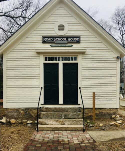 Historic Read School House with a white exterior, black doors, and stone steps, surrounded by bare trees.