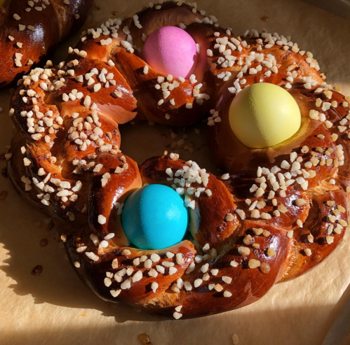 A braided sweet bread wreath topped with colorful eggs and sugar crystals, resting on parchment paper.