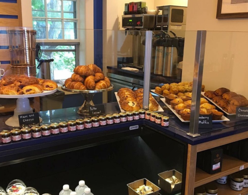 A display of freshly baked pastries, including croissants, muffins, and jars of jam, in a cozy café setting.