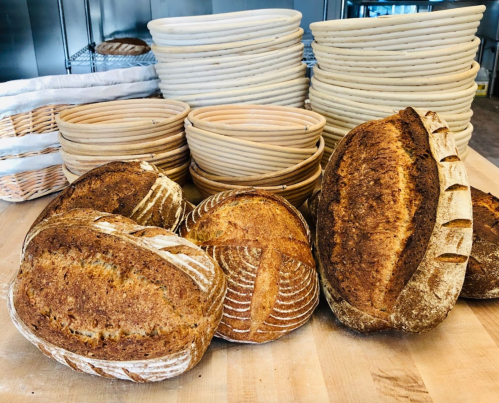 Freshly baked artisan breads displayed on a wooden surface, with proofing baskets stacked in the background.