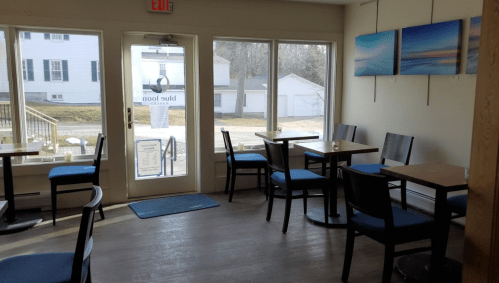 A cozy café interior with empty tables, large windows, and artwork on the walls, creating a welcoming atmosphere.