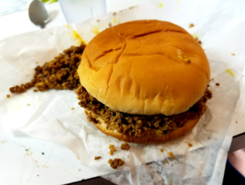 A messy sandwich with a soft bun filled with crumbled meat, resting on crumpled parchment paper.