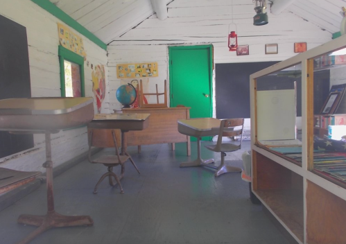 A vintage classroom with wooden desks, a globe, and chalkboards, featuring rustic white walls and green accents.