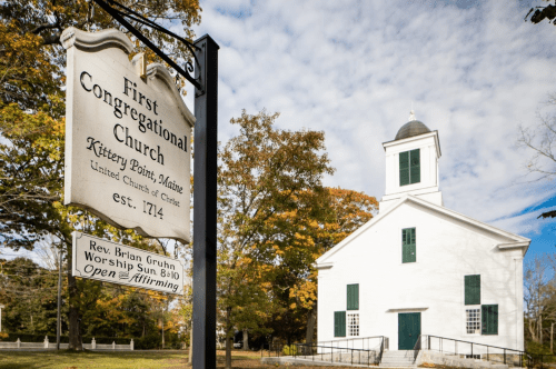Sign for First Congregational Church in Kittery Point, Maine, with a historic white building and autumn foliage.
