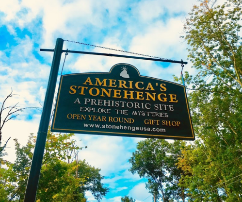 Sign for America's Stonehenge, a prehistoric site with a gift shop, open year-round, set against a cloudy sky.