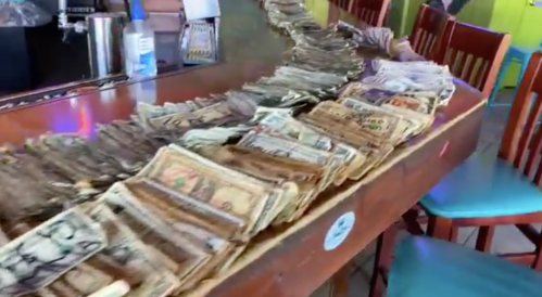 A long line of stacked cash on a bar counter, with colorful chairs in the background.