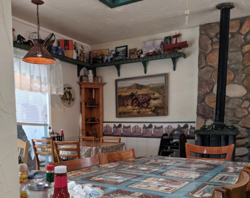 Cozy dining area with wooden tables, rustic decor, and a stone fireplace, featuring a western-themed painting.