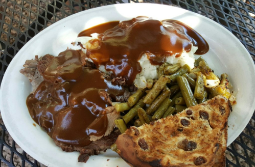 A plate of sliced beef with gravy, mashed potatoes, green beans, and a slice of toasted bread.