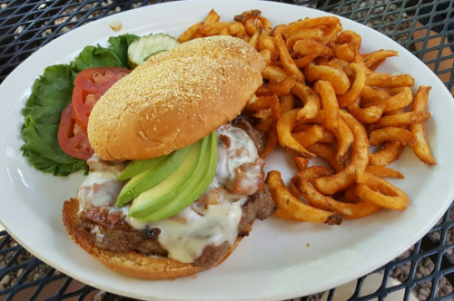 A juicy burger topped with cheese and avocado, served with curly fries and fresh lettuce, tomato, and cucumber on the side.