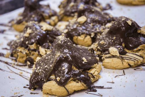 A close-up of cookies topped with chocolate and crushed graham crackers, arranged on parchment paper.