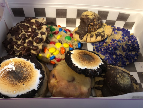 A box of assorted cookies, featuring chocolate chips, colorful candies, s'mores, and various toppings.