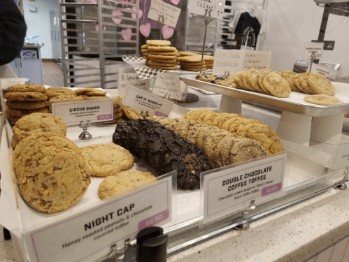 A display of various cookies, including Circus Snack, Night Cap, and Double Chocolate Coffee Toffee, in a bakery.