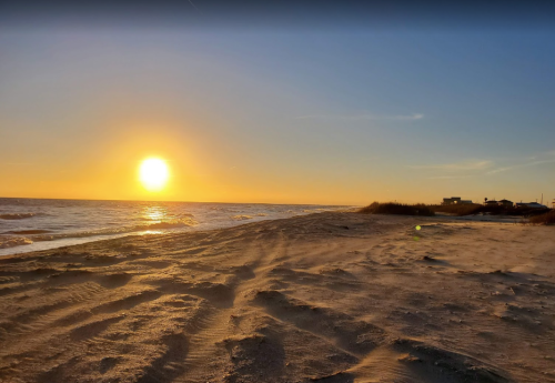 A serene beach at sunset, with golden light reflecting on the water and gentle waves lapping at the shore.