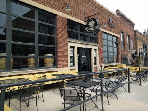 Exterior of a brick building with large windows, featuring outdoor seating and a sign that reads "Brewery."