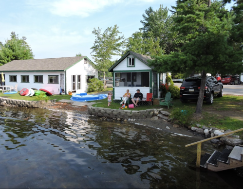 A lakeside scene with two cottages, a family relaxing by the water, and colorful kayaks nearby.