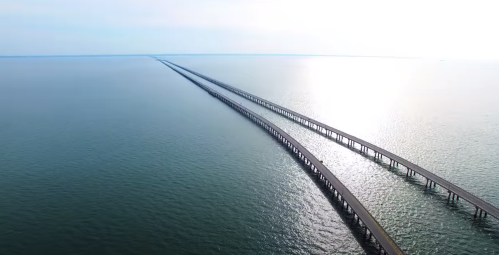 Aerial view of two parallel bridges extending over calm blue waters towards the horizon.