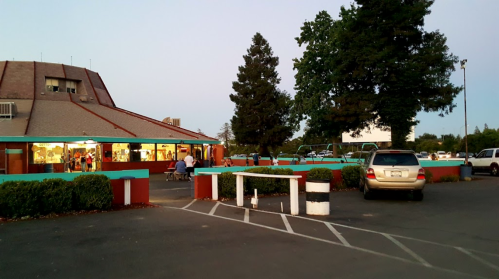 A colorful building with a parking lot at dusk, featuring people outside and a drive-in screen in the background.