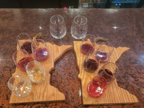 Two wooden trays shaped like Minnesota, each holding glasses of various wines and spirits.