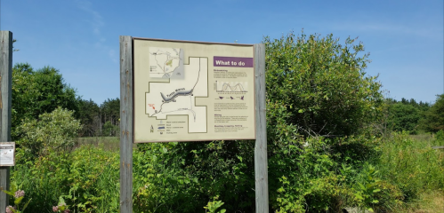A signpost in a natural area, displaying a map and information about activities and trails available nearby.