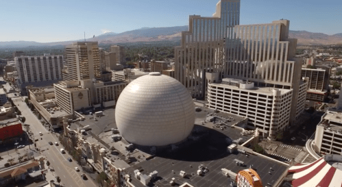 Aerial view of a city skyline featuring a large spherical building and modern skyscrapers under a clear blue sky.