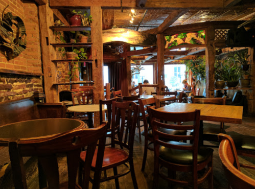 Cozy restaurant interior with wooden tables, chairs, and plants, featuring warm lighting and a rustic atmosphere.