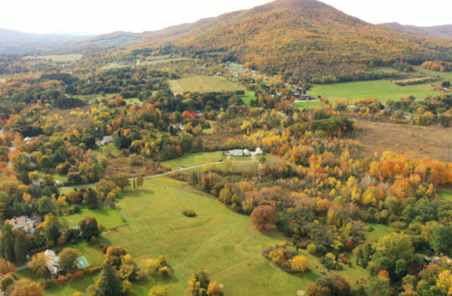Aerial view of a colorful autumn landscape with rolling hills, trees, and scattered homes.