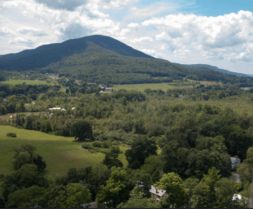 A panoramic view of a lush green landscape with rolling hills and a mountain under a partly cloudy sky.