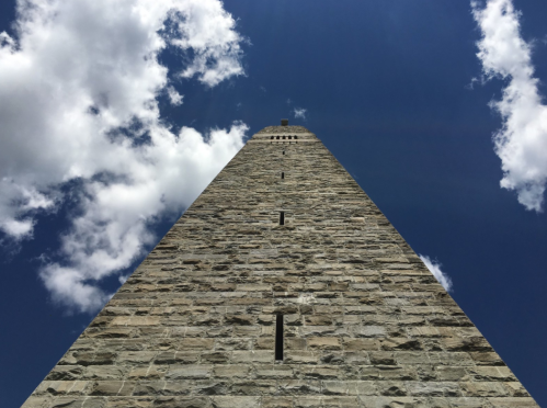 A tall stone tower reaching towards a blue sky with fluffy white clouds.