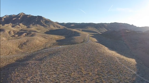 Aerial view of a desert landscape with rolling hills and a winding road under a clear blue sky.