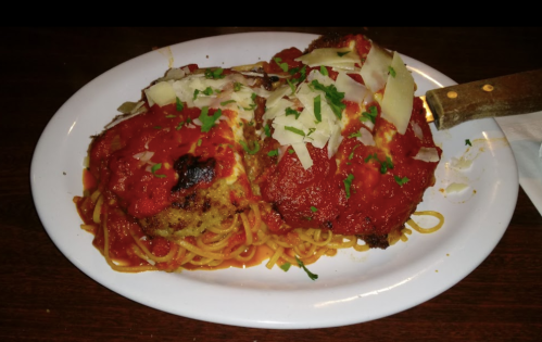A plate of spaghetti topped with two breaded chicken cutlets, marinara sauce, and grated cheese, garnished with parsley.