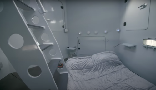 A minimalist, futuristic room with a bed, stairs, and circular windows, featuring a sleek, white design.