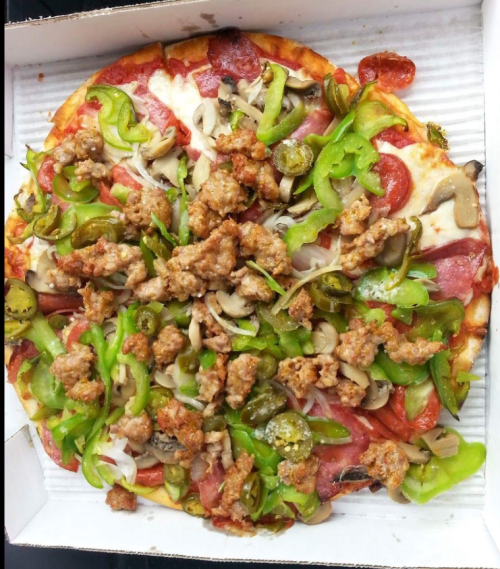 A pizza topped with pepperoni, sausage, green peppers, onions, mushrooms, and jalapeños in a takeout box.
