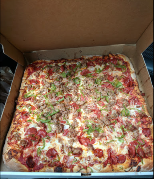 A large pizza topped with pepperoni, sausage, green peppers, and onions in a cardboard box.