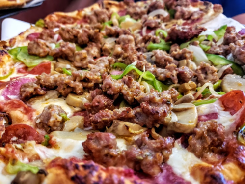 Close-up of a pizza topped with sausage, green peppers, onions, and mushrooms on a crispy crust.