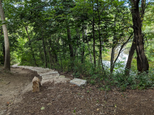 A winding path through lush greenery, leading to a river with a waterfall in the background.