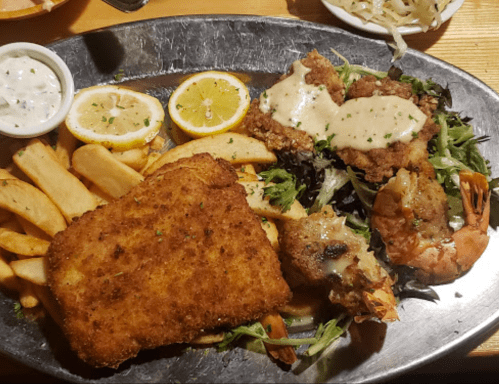A platter featuring fried fish, shrimp, and crab cakes, served with fries, salad, and lemon slices.
