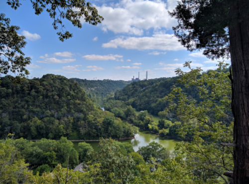 A scenic view of a river winding through green hills under a blue sky with scattered clouds.