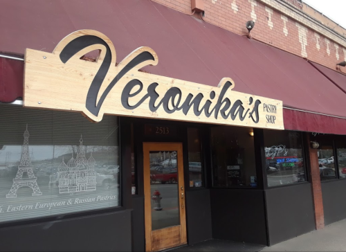 Sign for Veronika's Pastry Shop, featuring a wooden design and a maroon awning, with decorative window graphics.
