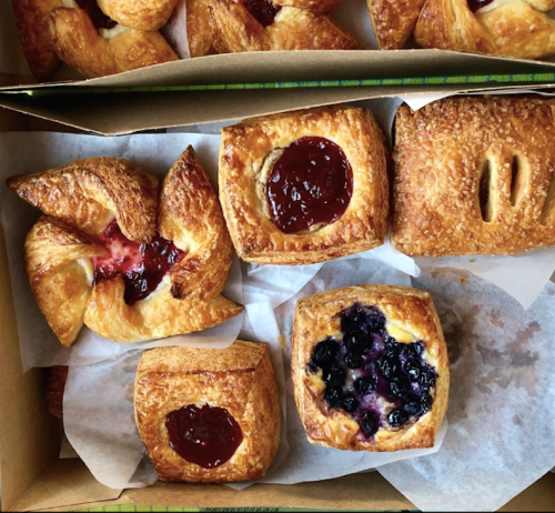 A box of assorted pastries, including fruit-filled danishes and a blueberry tart, on parchment paper.