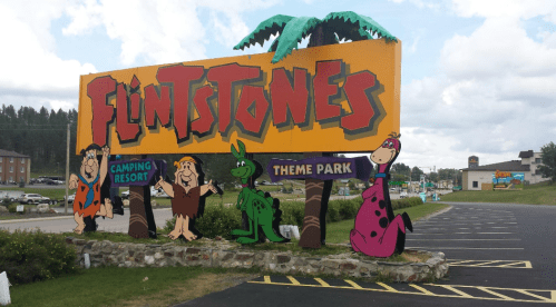 Colorful sign for the Flintstones Camping Resort and Theme Park, featuring characters like Fred, Barney, and Dino.