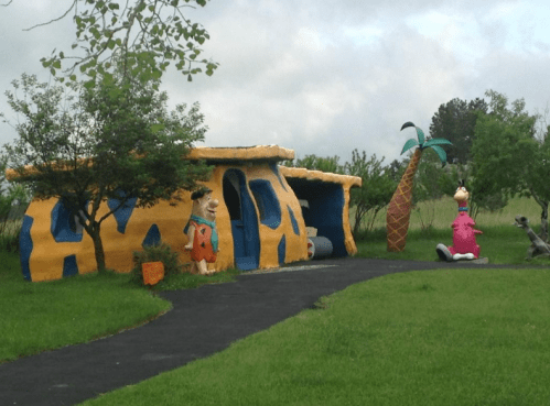 A colorful, cartoon-style house resembling the Flintstones' home, with characters and palm trees in a grassy area.