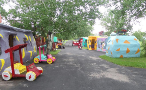 Colorful, cartoonish houses and vehicles line a pathway in a whimsical, themed outdoor setting.