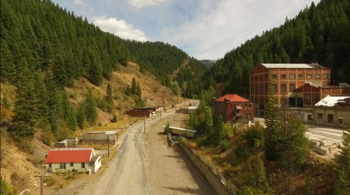 Aerial view of a deserted mining town surrounded by lush green mountains and a clear blue sky.