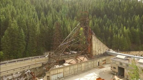 An abandoned mining structure surrounded by dense green forest, with rusted metal and concrete remnants visible.