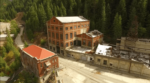Aerial view of abandoned brick buildings surrounded by dense green forest.