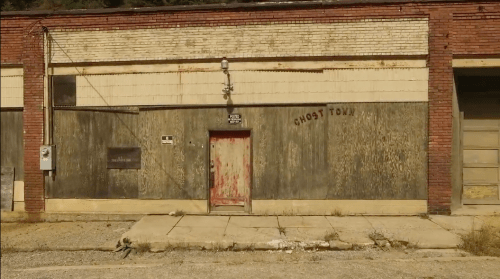 Abandoned building with a weathered facade, featuring a red door and the words "GHOST TOWN" on the wall.