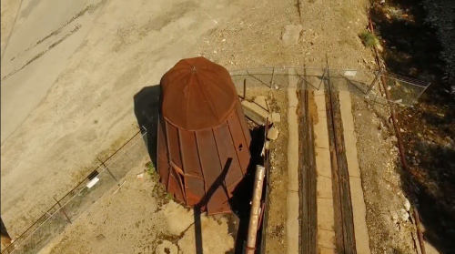 Aerial view of a rusted, octagonal structure surrounded by barren land and railway tracks.